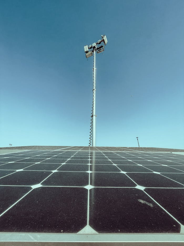 Solar panels under a clear blue sky with a communication tower in the background.